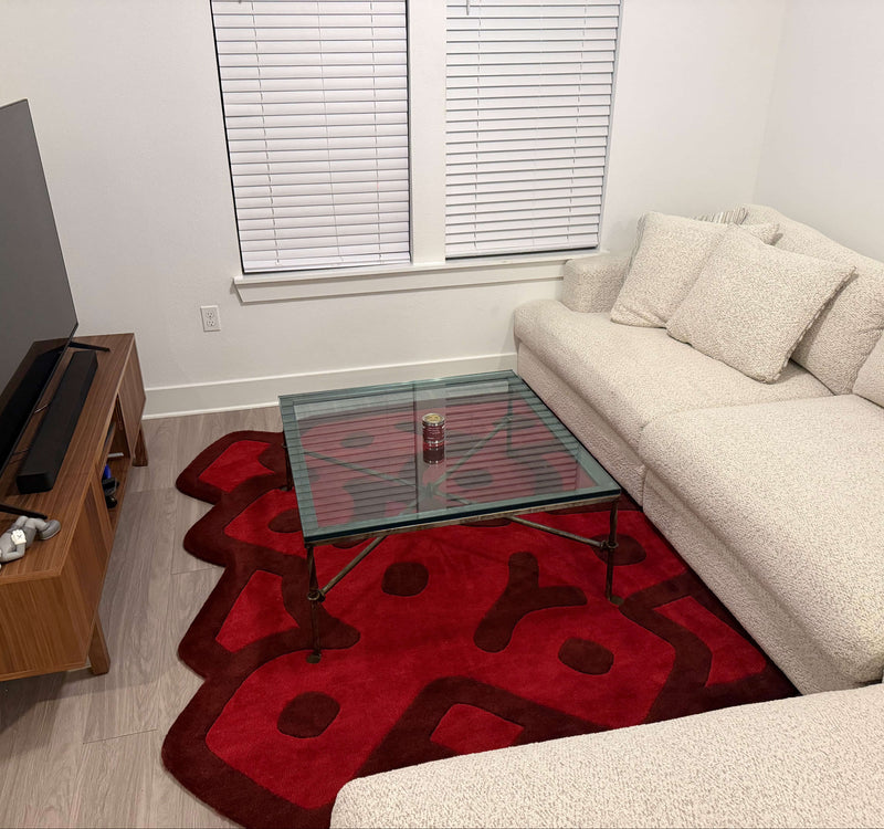 Living room with a beige sectional sofa, red rug, glass coffee table, and TV stand.